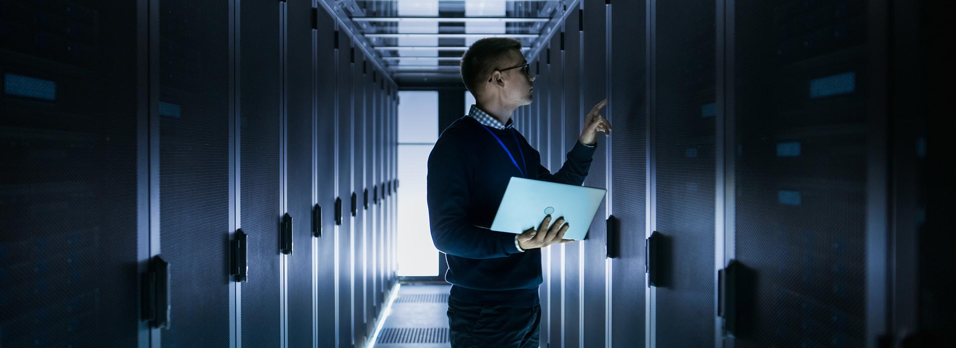 A darkened image of a man with a laptop inside a server room